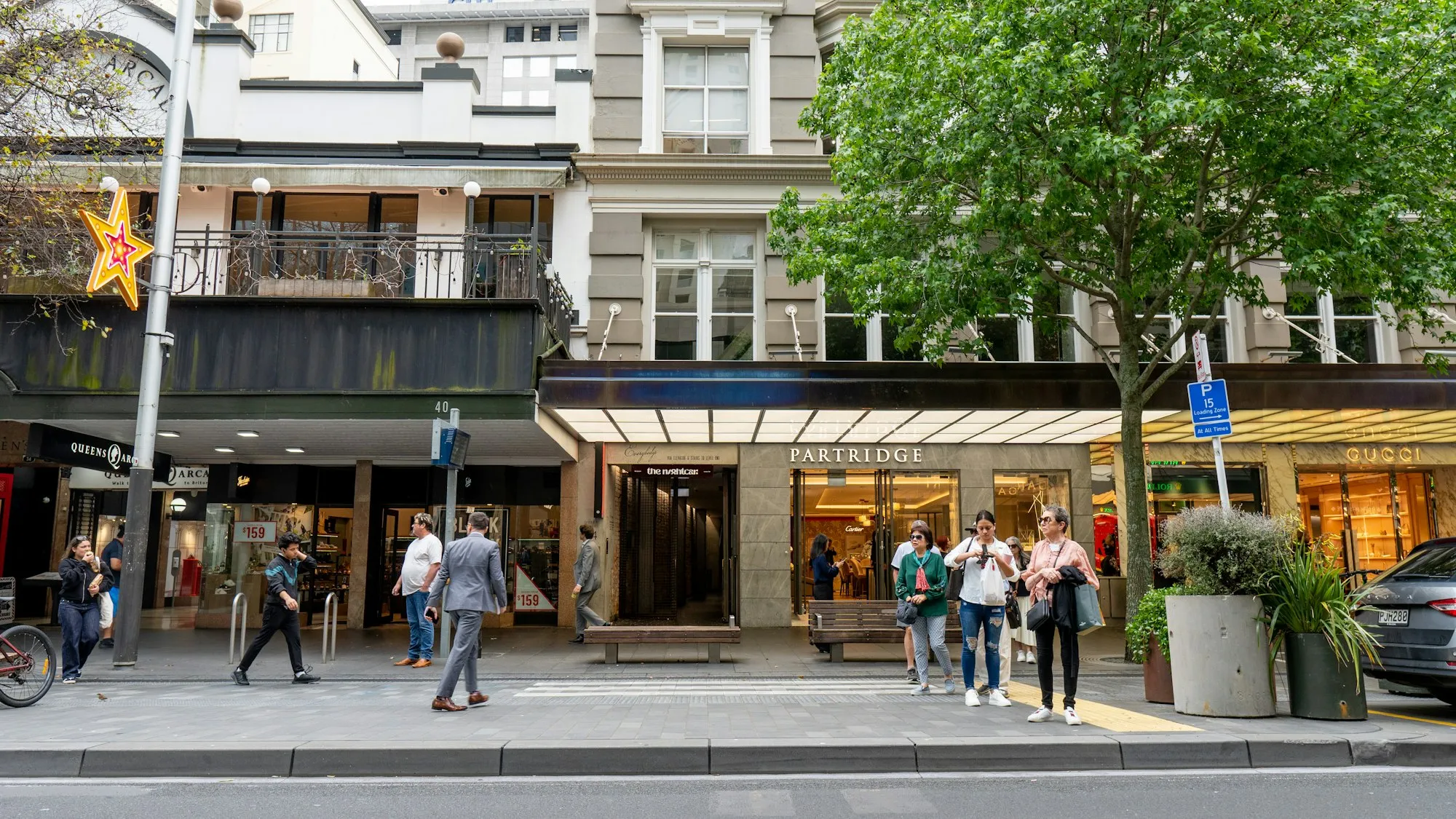 Shoppers on the footpath outside a row of shops on an Auckland street